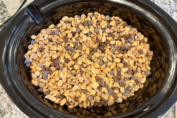 Adding peanuts, peanut chips, and chocolate chips into a crockpot.