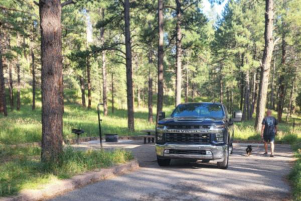 The photo shows a truck parked in campsite to help the reader determine whether RV or tent camping is better.